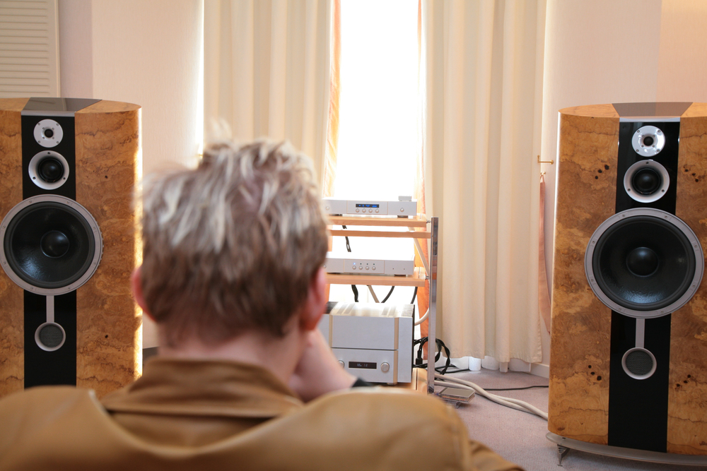 Homme écoutant de la musique à la maison sur un système HIFI avec des enceintes en bois haut de gamme